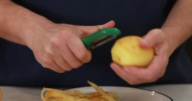 Bir adam çiğ patatesleri bıçakla soyar. Yemek pişirme süreci. Video Talimatları