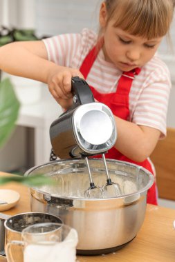 Önlüklü sarışın kız krep hamurunu elektrikli mikserle dövüyor. Mutlu genç ev hanımı evde, mutfakta aile için güzel bir kahvaltı hazırlıyor.