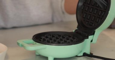 Ev fırıncısı waffle ızgarasını yağlar ve hamuru dökmeden önce kaplamayı sağlar. Kadın aşçı kapağın üstüne çiğ hamur dökerek mükemmel altın ve çıtır waffle yapıyor.