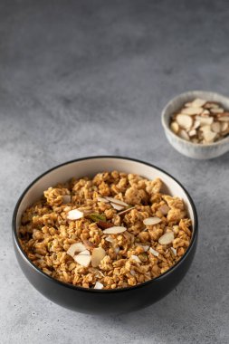 Siyah bir kasede dilimlenmiş bademle birlikte gri arka planda gevrek ev yapımı granola. Sağlıklı yemek için ideal.