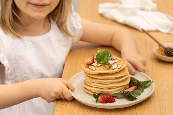 stock image The todler girl holds a plate with delicious pancakes for breakfast at the table. Handmade dish