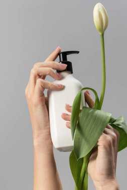 Kadın arka planda beyaz lale ve şişeyi yakın plan çekimde kullanıyor. Vücut yıkama kozmetik ürünü model şablonla. Boş ambalaj
