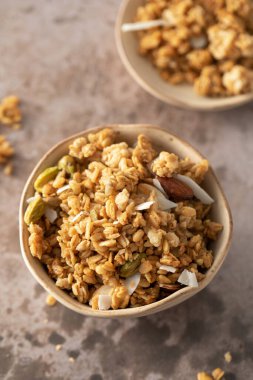 Siyah bir kasede dilimlenmiş bademle birlikte kahverengi arka planda gevrek ev yapımı granola. Sağlıklı yemek için ideal.