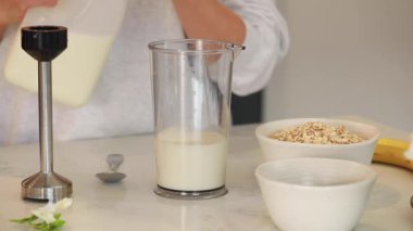 Beslenme uzmanı yulaf ezmesi ve chia tohumlarını karıştırıcıya döküyor. Kadın enerji ve vitaminlerle yeni bir güne başlamak için besin yoğunluğunda smoothie hazırlıyor.