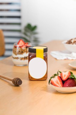 Boş etiketli bal kavanozu, ahşap masada çilek ve balık. Mutfakta sağlıklı atıştırmalıklar bulunan doğal tatlı şurup. Diyet reklamları için ürünler