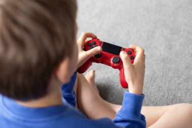 Çocuk elinde bir joystick tutuyor ve dikkatle bir video oyunu oynuyor. Video oyunları konsepti, bir oyun konsolu.