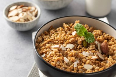 Siyah bir kasede dilimlenmiş bademle birlikte gri arka planda gevrek ev yapımı granola. Sağlıklı yemek için ideal.