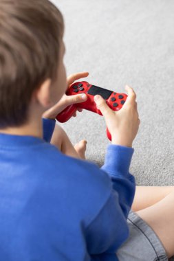 Çocuk elinde bir joystick tutuyor ve dikkatle bir video oyunu oynuyor. Video oyunları konsepti, bir oyun konsolu.