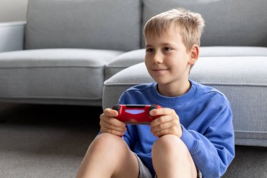Çocuk elinde bir joystick tutuyor ve dikkatle bir video oyunu oynuyor. Video oyunları konsepti, bir oyun konsolu.