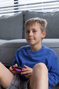 Çocuk elinde bir joystick tutuyor ve dikkatle bir video oyunu oynuyor. Video oyunları konsepti, bir oyun konsolu.