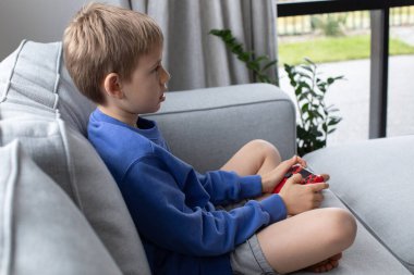 Çocuk elinde bir joystick tutuyor ve dikkatle bir video oyunu oynuyor. Video oyunları konsepti, bir oyun konsolu.