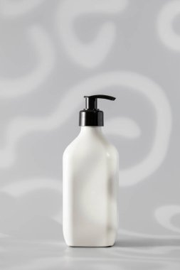 Ürün sunumu için yumuşak soyut arka planda siyah kapaklı minimalist bir beyaz pompa şişesi. Kozmetik ürünü olan bir düzen