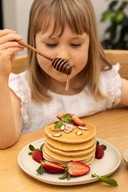 Küçük kız taze kreplere taze çilek ve fındıklı bal ekler. Sevimli çocuk ev mutfağındaki krep yığınına tatlı şurup döküyor. Sağlıklı beslenme