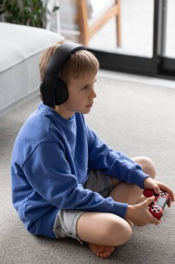 Mavi kazaklı, kulaklık takan, oturma odasındaki video oyununa odaklanmış genç bir çocuk. Oyun konsolları, video oyunları konsepti