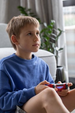 Çocuk elinde bir joystick tutuyor ve dikkatle bir video oyunu oynuyor. Video oyunları konsepti, bir oyun konsolu.