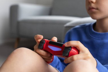 Çocuk elinde bir joystick tutuyor ve dikkatle bir video oyunu oynuyor. Video oyunları konsepti, bir oyun konsolu.
