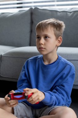 Çocuk elinde bir joystick tutuyor ve dikkatle bir video oyunu oynuyor. Video oyunları konsepti, bir oyun konsolu.