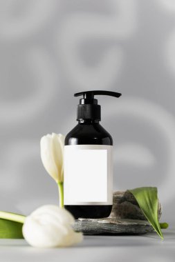 Taş podyumda kozmetik malzemeli şeker şişesi. Cilt temizleme kozmetik ürün paketi hafif arka planda yumuşak beyaz çiçek