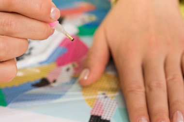 Yaratıcılık ve rahatlamayı gösteren bir elmas resim projesi için minicik kristalleri tuvale yerleştiren bir elin yakın çekimi. Elmas Mozaiği