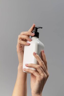 Kadın elleri, üzerinde boş etiket olan bir şişe gösteriyor. Cilt Bakımı Konsepti