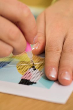 Yaratıcılık ve rahatlamayı gösteren bir elmas resim projesi için minicik kristalleri tuvale yerleştiren bir elin yakın çekimi. Elmas Mozaiği