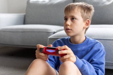 Çocuk elinde bir joystick tutuyor ve dikkatle bir video oyunu oynuyor. Video oyunları konsepti, bir oyun konsolu.