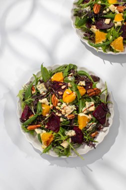 Pancar kökü ve portakal dilimli lezzetli salata beyaz masada gölge desenli servis edilir. Öğle yemeği için sebze, meyve ve peynir tabağı.