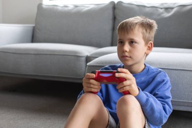 Çocuk elinde bir joystick tutuyor ve dikkatle bir video oyunu oynuyor. Video oyunları konsepti, bir oyun konsolu.
