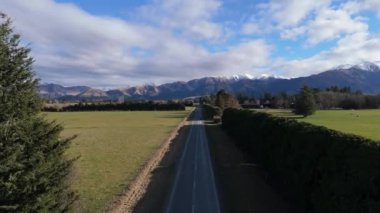 Yol, tarlalar ve sıra sıra ağaçlarla çevrili dağ sırasına doğru uzanıyor. Çiftçilik alanlarında seyahat etmeyi yansıtan ekinlerin büyümesi için belirlenmiş bitişik araziler