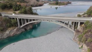 Sürücü arabalı ulaşım köprüsü nehir kıyısında donmuş suyla kesişiyor. Ağır gökyüzü, sakin bahar manzarasının üzerinde asılı duruyor. Dağlık bölgelerin güzelliği