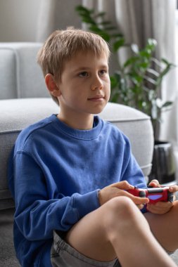 Çocuk elinde bir joystick tutuyor ve dikkatle bir video oyunu oynuyor. Video oyunları konsepti, bir oyun konsolu.