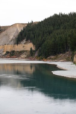 Huzurlu Rakaia nehri dik kıyı şeridini ve çam ağaçlarını geçer. Resimli vadi Yeni Zelanda 'da ünlü turistik bir yer. Muhteşem vahşi doğa.