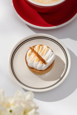 Beyaz arka planda küçük kremalı pasta ve kahve fincanı. Masa yüzeyinde kafein içeren lüks bir tatlı. Kahve dükkanı ürünleri.