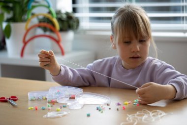 Tatlı bir kız coşkuyla boncuklardan bir bilezik yapıyor, bir sürü renkli boncuk diziyor. Mücevher yapan yaratıcı bir çocuk..