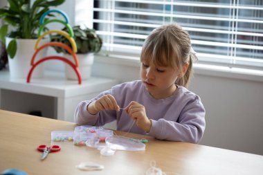Tatlı bir kız coşkuyla boncuklardan bir bilezik yapıyor, bir sürü renkli boncuk diziyor. Mücevher yapan yaratıcı bir çocuk..