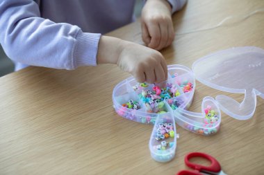 Bir kız coşkuyla boncuklardan bir bilezik yapıyor, bir sürü renkli boncuk diziyor. Mücevher yapımında çalışan yaratıcı bir çocuk. Kapat.