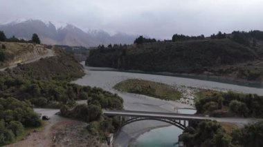 Sürücü arabalı ulaşım köprüsü nehir kıyısında donmuş suyla kesişiyor. Ağır gökyüzü, sakin bahar manzarasının üzerinde asılı duruyor. Dağlık bölgelerin güzelliği
