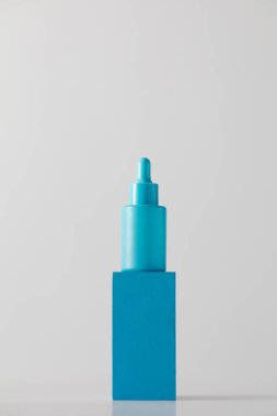 Beyaz arka planda podyumda yaşlanmayı önleyici serumu olan mavi damlatıcı. Kozmetik konsepti, cilt bakımı.