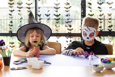 Cadılar Bayramı kostümlü şirin erkek ve kız kardeşler masada şenlikli el sanatları yapıyorlar. Cadılar Bayramı el sanatları üzerine bir master sınıfı. Mutlu Cadılar Bayramı.