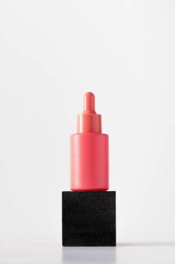 Beyaz arka planda podyumda yaşlanmayı önleyici serumu olan pembe damlalar. Kozmetik konsepti, cilt bakımı.