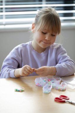Tatlı bir kız coşkuyla boncuklardan bir bilezik yapıyor, bir sürü renkli boncuk diziyor. Mücevher yapan yaratıcı bir çocuk..