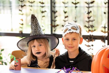 Karnaval kostümlü tatlı bir oğlan ve kız bir masada oturup Cadılar Bayramı kutlamaları için el işi yapıyorlar. Mutlu Cadılar Bayramı.