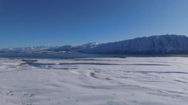 Tekapo Gölü soğuk kış günlerinde güzelliğe hayrandır. Turkuaz su ve göl kıyısının dağlara karşı beyaz karla kaplı büyüleyici manzarası.