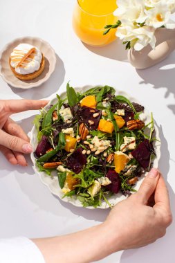 Lezzetli salatası ve portakal suyu olan bir kadın beyaz masada oturuyor. Kadın güneşli bir sabahta besleyici vegan yemeği yer. Sağlıklı tayın