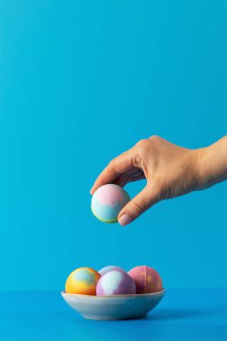 Kadın, mavi arka plandaki banyo tezgahına konmuş renkli banyo bombasını kaseden alıyor. Küveti rahatlatıcı aroma ve kabarcıklarla doldurmak için tasarlanmış banyo bombaları.