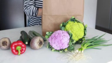 Bir kadın mutfaktaki kese kağıdından çeşitli olgun sebzeleri alıyor. Evinize taze sebze götürme fikri.