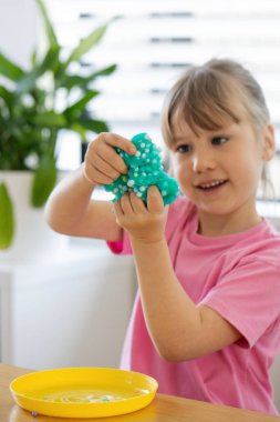 A child playing with bright, blue slime, enjoying a fun and creative indoor activity. Childhood, craft. clipart