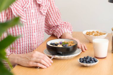 Bir kadın masada oturuyor ve sağlıklı bir kahvaltı yapıyor. Yunan yoğurdu ve yabanmersinli granola. Kahvaltı kavramı