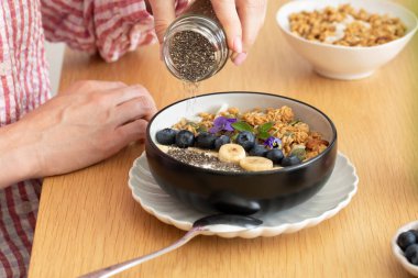 Bir kadın granola ve Yunan yoğurduna chia tohumu döküyor. Sağlıklı kahvaltı kavramı.