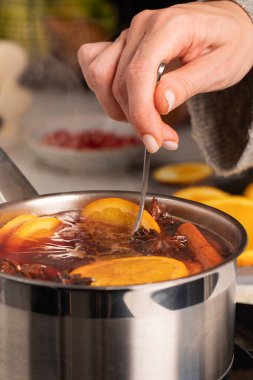 Bir kadın mutfaktaki bir tencerede kaşıkla kaynamış şarap karıştırıyor. Ilık bir içecek hazırlama süreci.